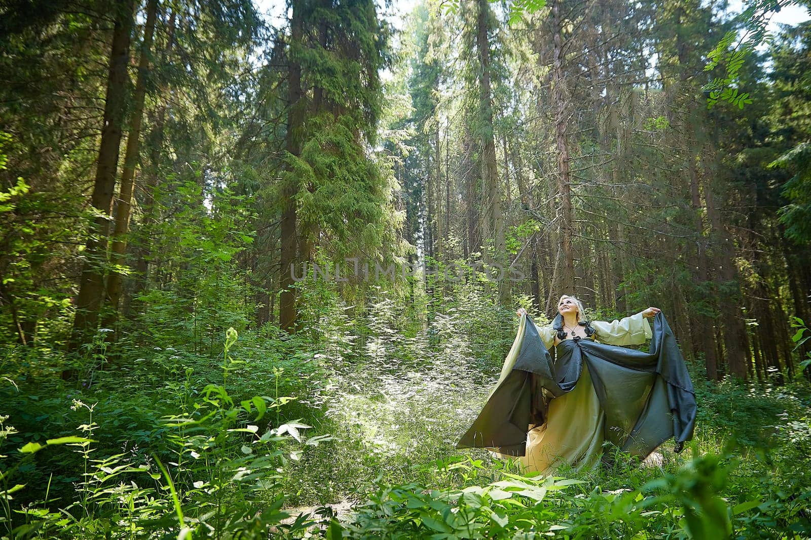 Adult mature woman 40-60 in a green long fairy dress in forest. Photo shoot in style of dryad and queen of nature. Fairy in beautiful green summer forest. Concept of caring for nature