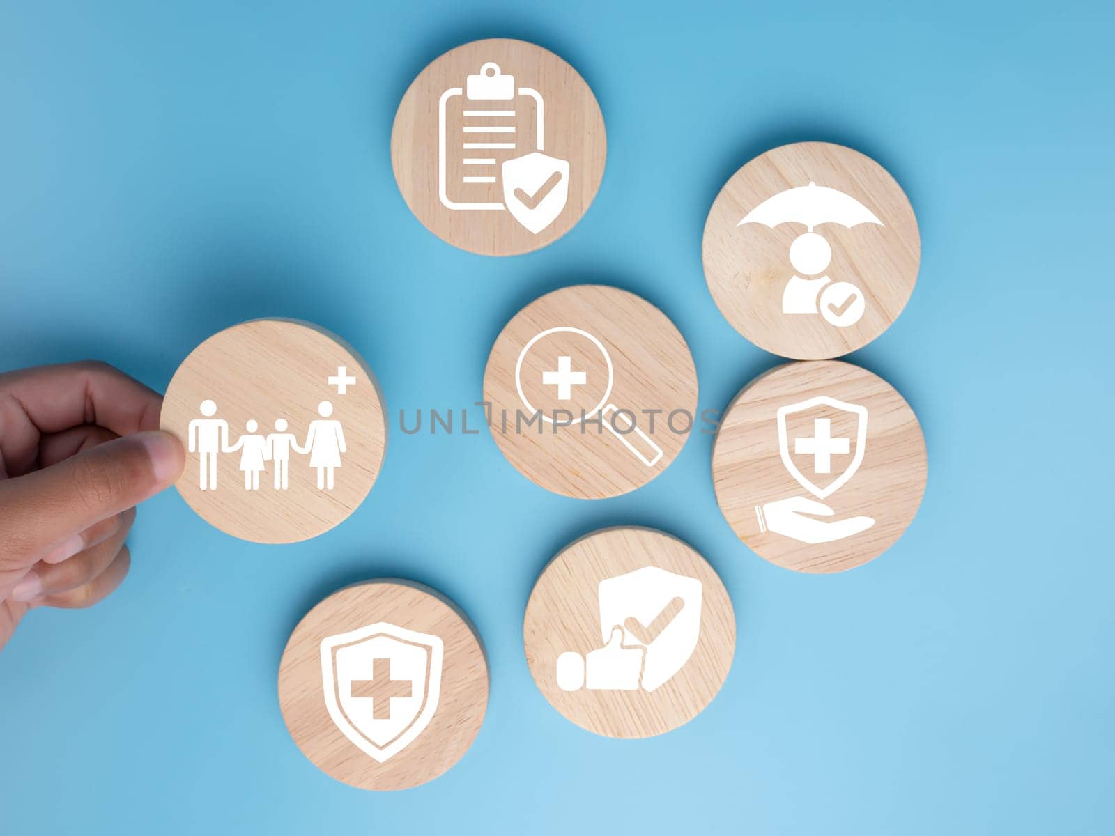 Health and medical concept, Human hand holds a wood circle with icons about health and access to treatment and medicine and supplies on a blue background.