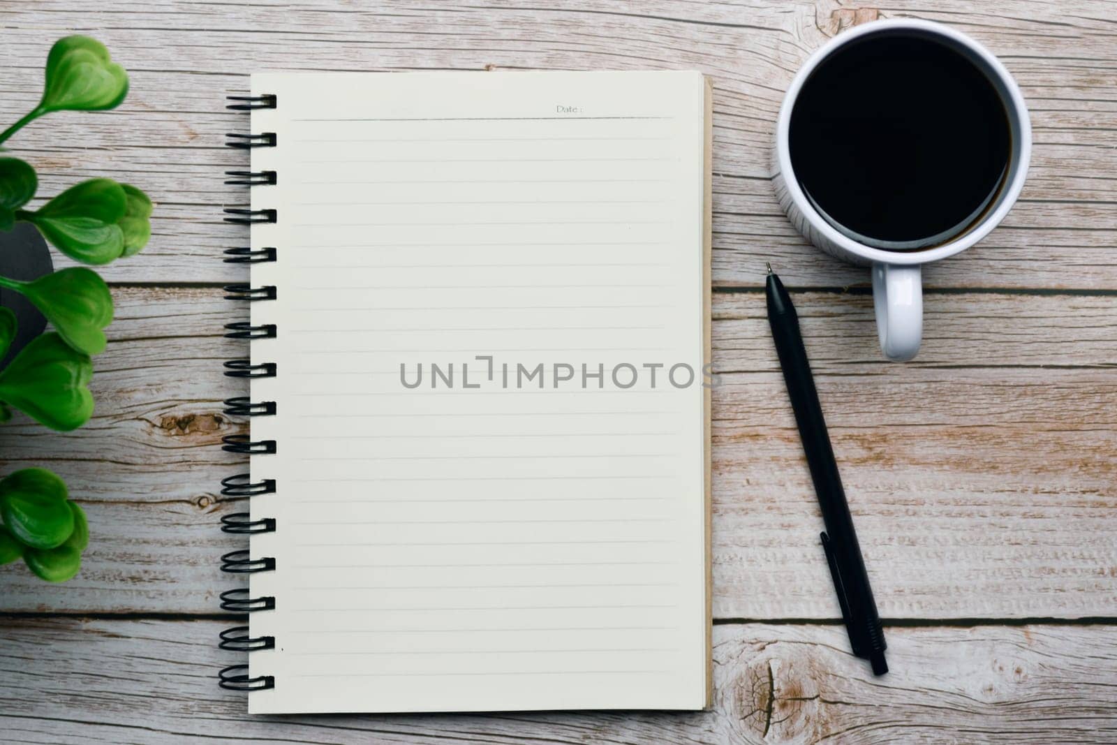 Directly above view of a desk with pen, notepad, plant and coffee. Flat lay. Copy space.