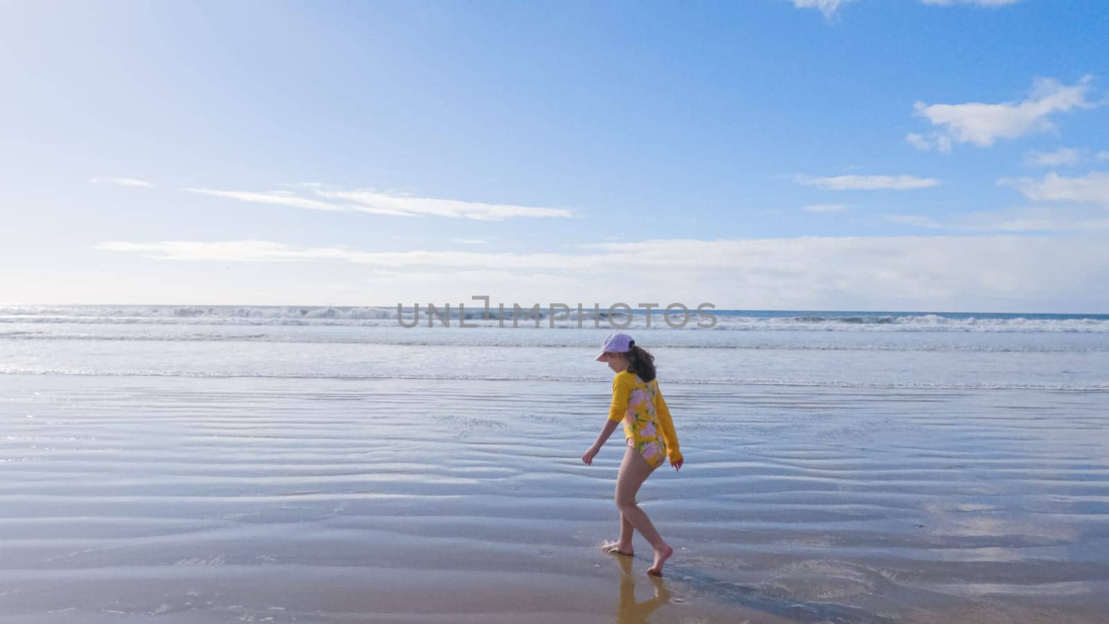 Little girl, braving the cold, joyfully runs in her swimsuit across the beach during winter.