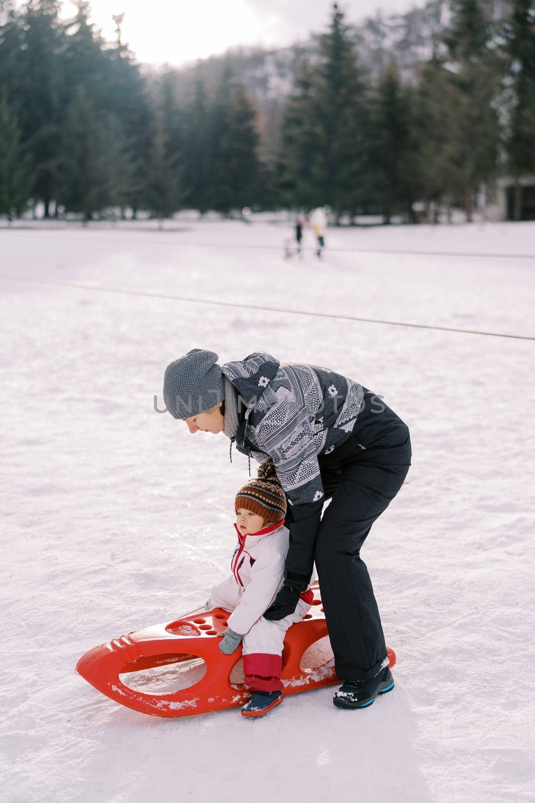 Mom puts a little girl on a sled on a snowy lawn. High quality photo