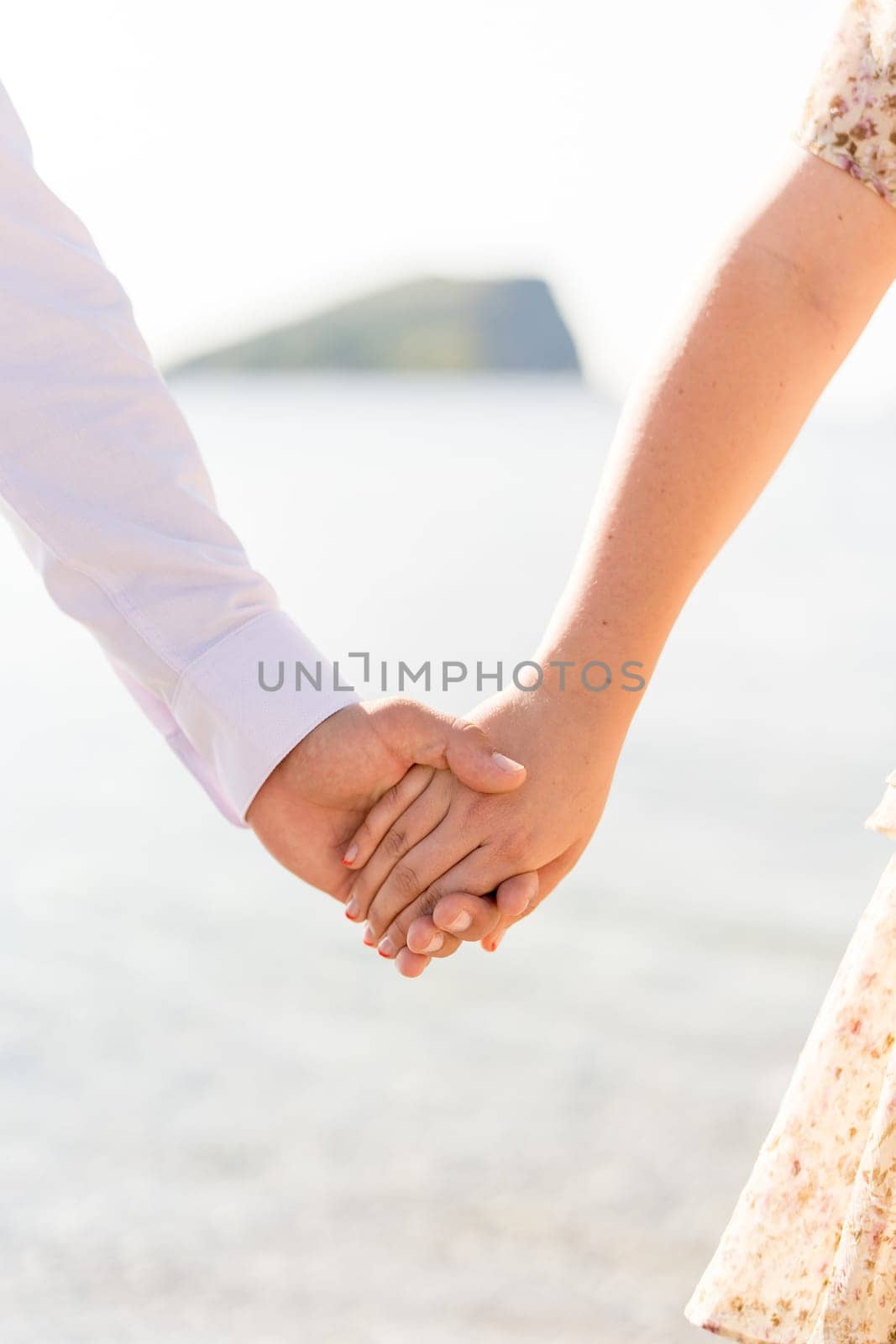 Man holds woman hand while standing on the seashore. Cropped. Faceless by Nadtochiy