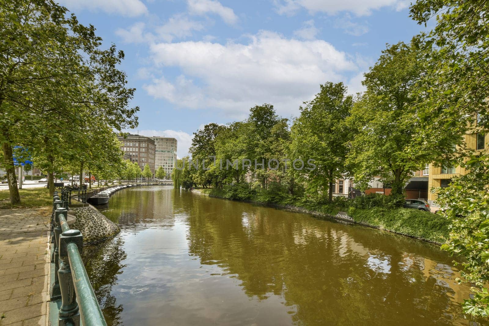 a canal with trees and buildings in the background, taken from a bridge over the water's edge on a sunny day