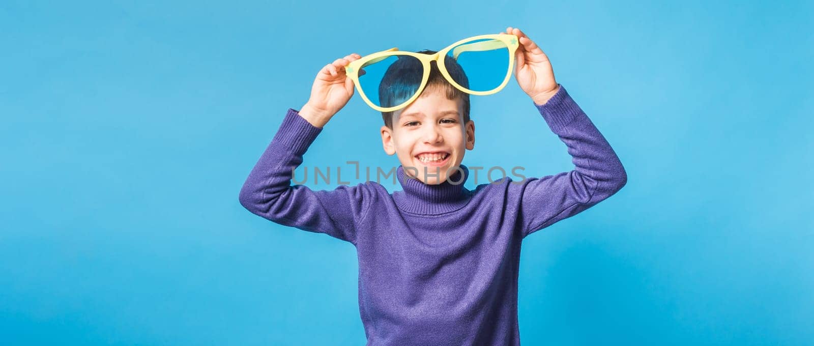 Cheerful little boy generation alpha in big glasses express a surprised face holds mockup board isolated on blue background with copy space.