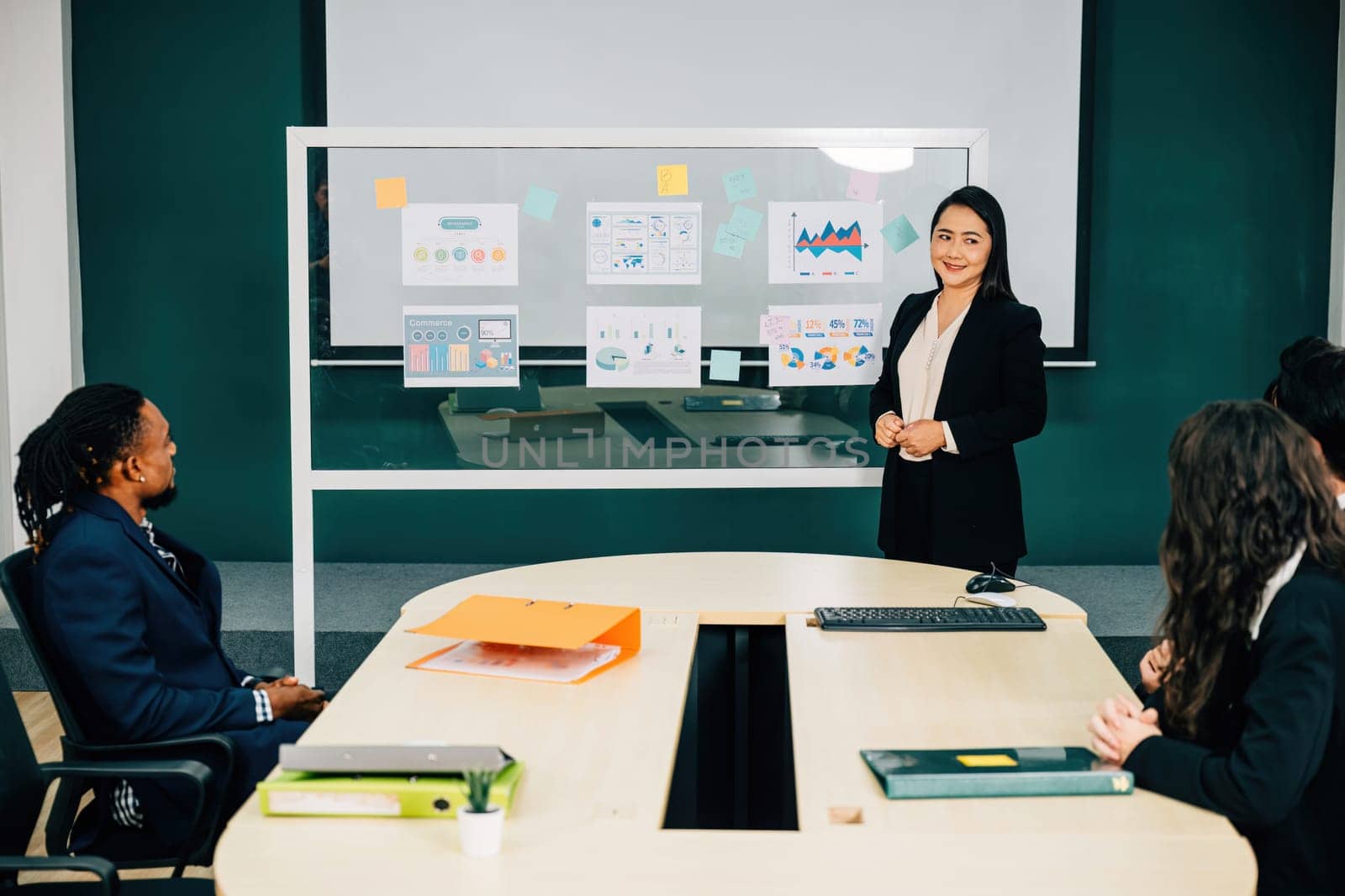 Businesswoman expert in finance and marketing, leads seminar in office conference room. She explains innovative e-commerce strategy, encouraging discussion, cooperation, diversity among colleagues. by Sorapop