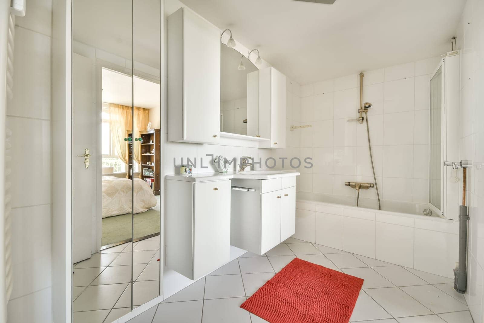 a white bathroom with a red rug on the floor and a large mirror in the corner to the shower stall