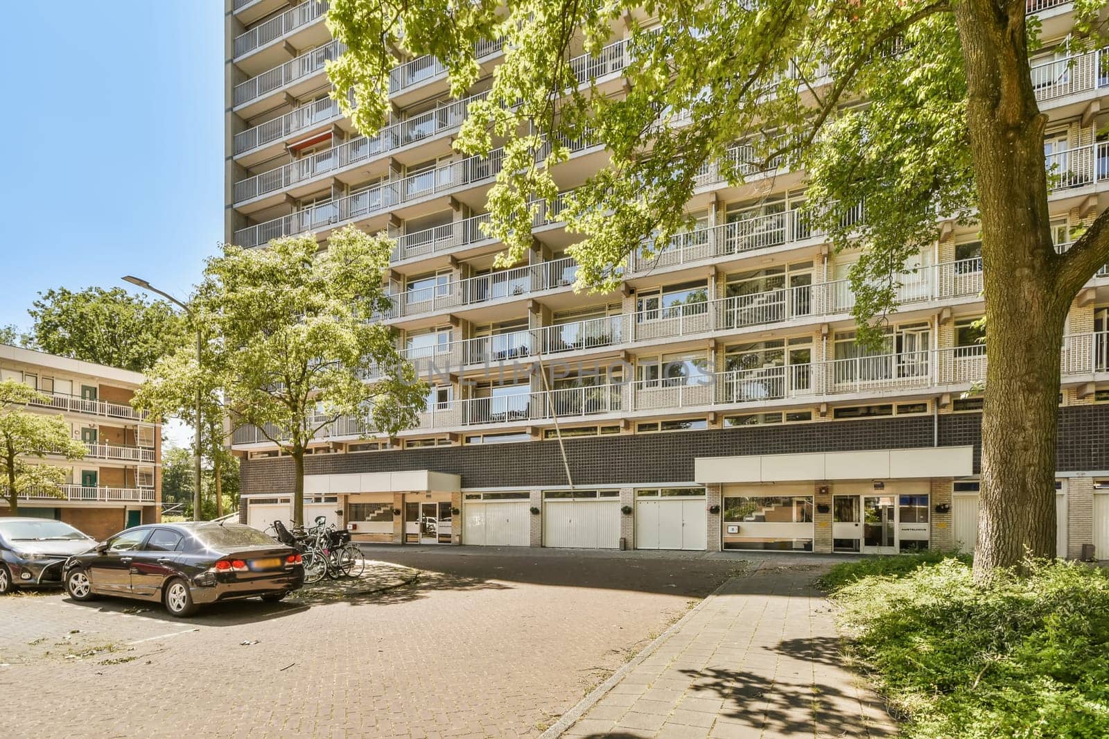 an apartment building with cars parked in the parking lot next to it and some trees on either side of the street