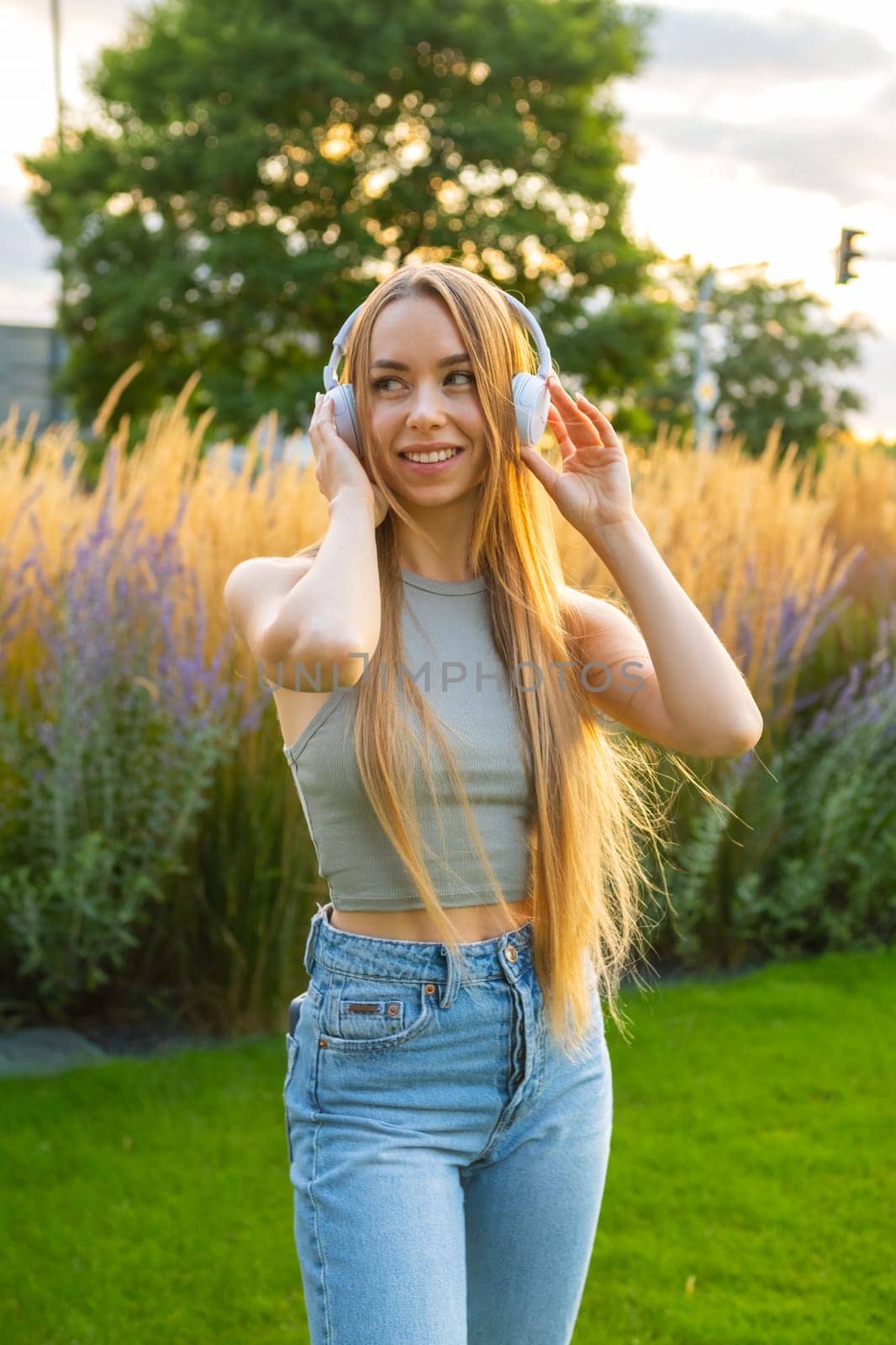 Portrait of a cheerful stylish young woman listen to the music using headphones in the park,