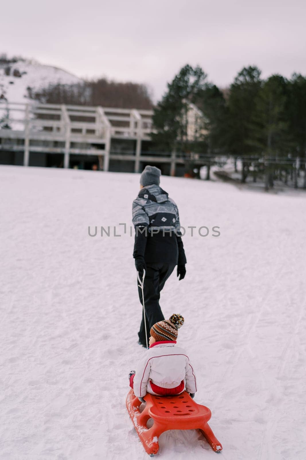 Mom carries a small child on a sled up the slope. Back view. High quality photo