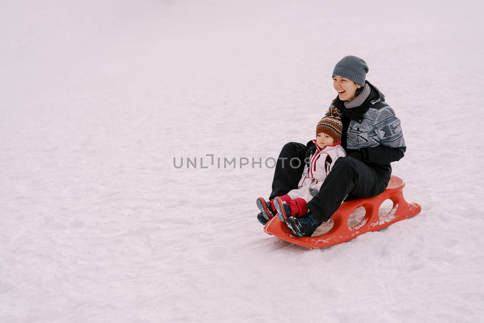 Laughing mother with a little girl ride a sleigh on a snowy hill. High quality photo