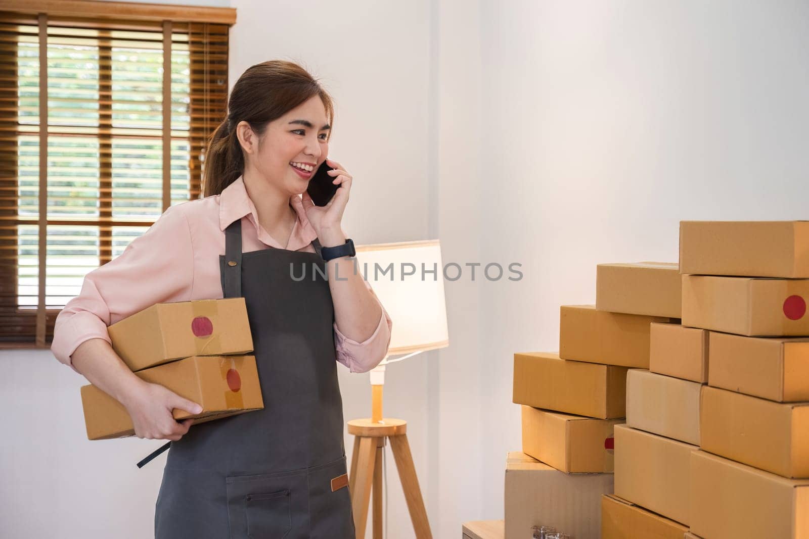 SME business owner A female entrepreneur uses a mobile phone to talk and work on boxes of merchandise. Receipts and checks online orders to prepare boxes for sale to customers..