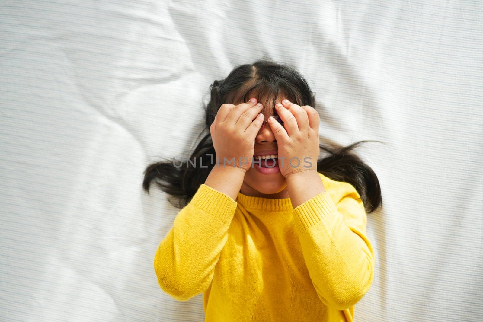a upset child girl cover her face with hand lying on the bed by towfiq007