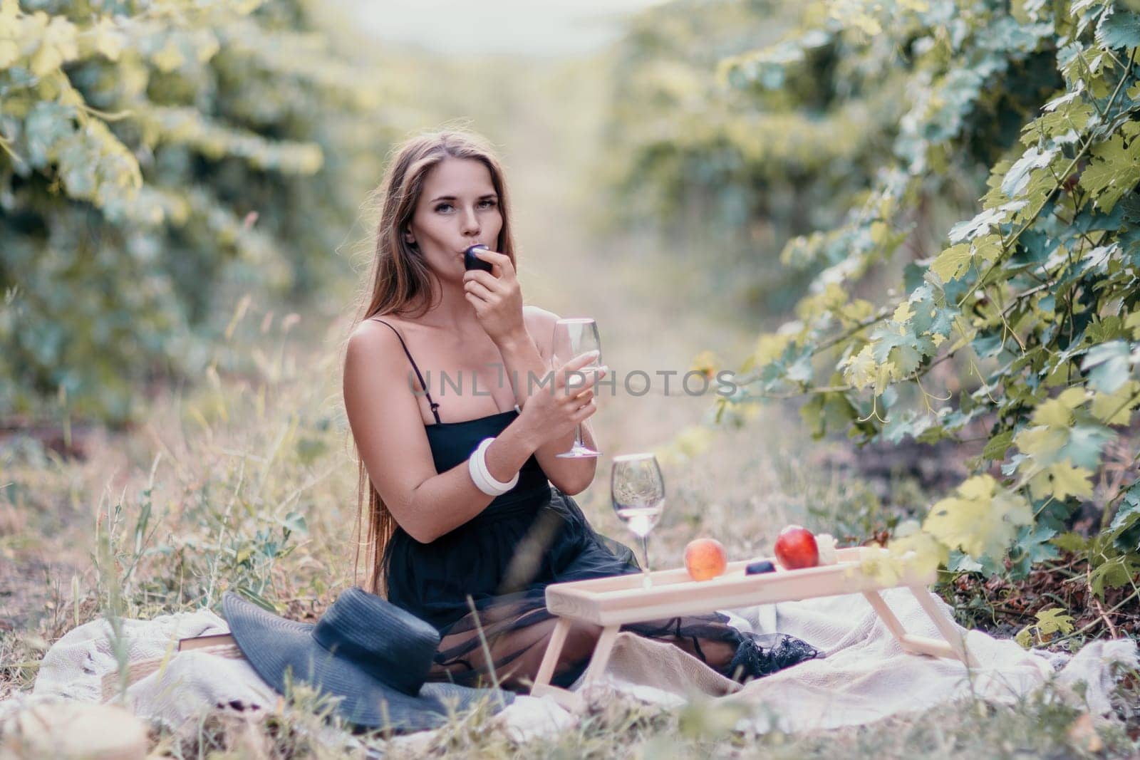 Woman picnic vineyard. Happy woman with a glass of wine at a picnic in the vineyard, wine tasting at sunset and open nature in the summer. Romantic dinner, fruit and wine. by panophotograph