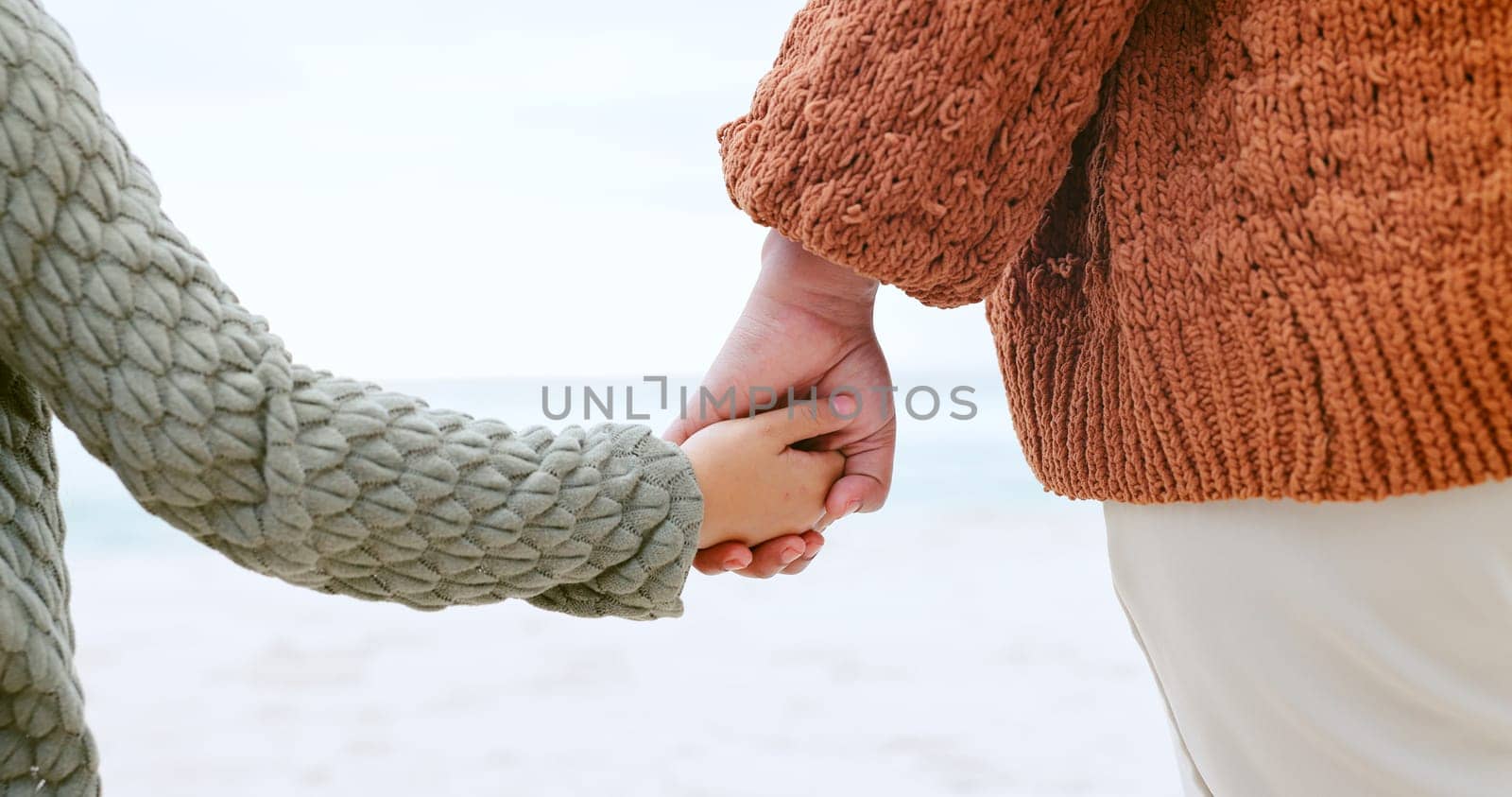 Parent, child and holding hands at ocean for love, care or support in trust, travel or outdoor getaway. Closeup of person with kid for unity, bonding or compassion on beach or sea coast together by YuriArcurs