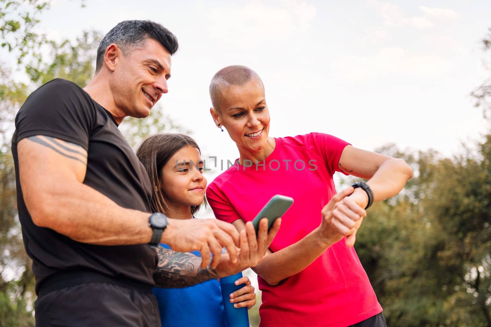 sporty family using a mobile phone and smart watch to plan their sports training in the countryside, concept of sport with kids in nature and active lifestyle, copy space for text