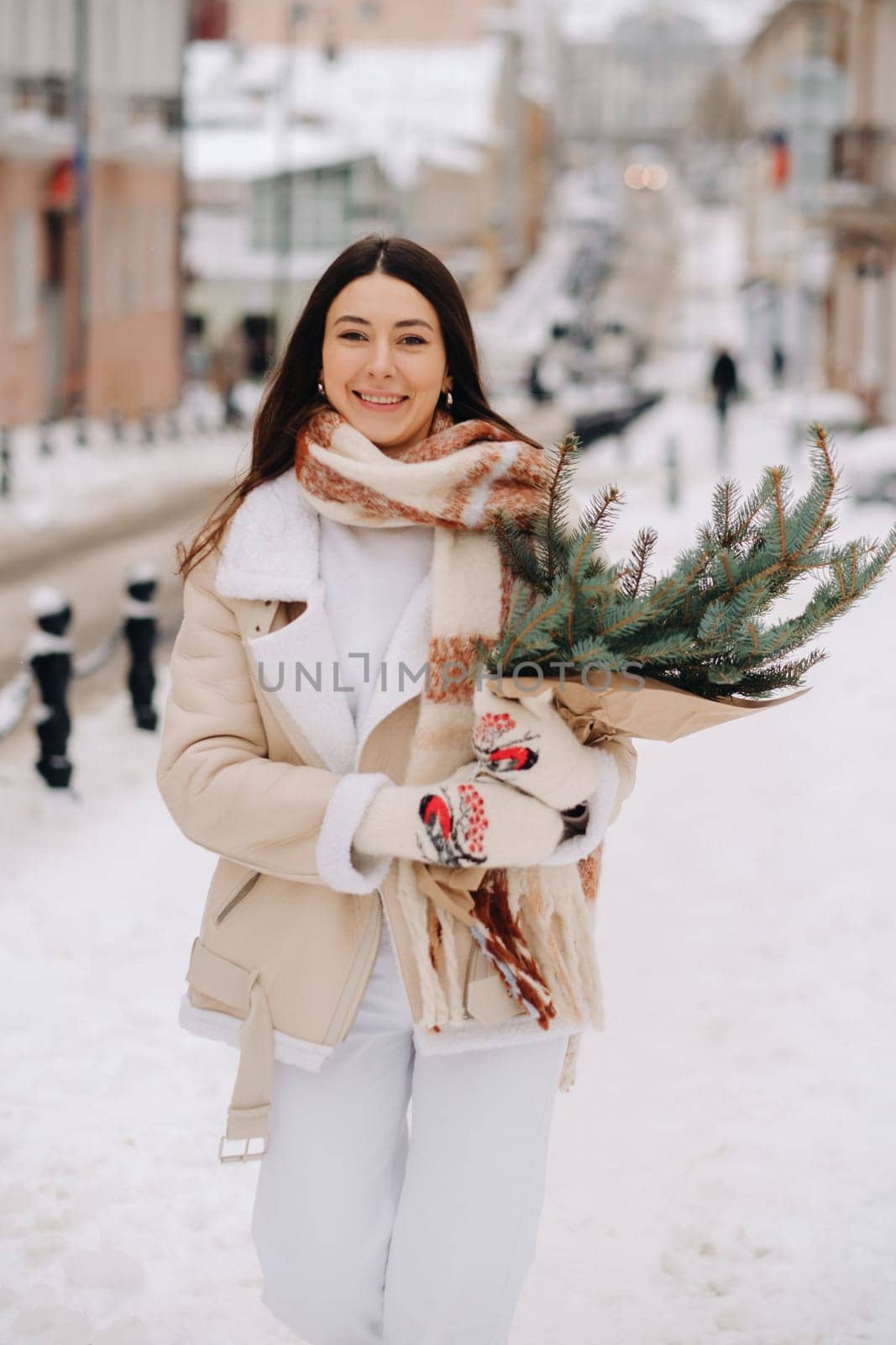 A girl with long hair in winter on the street with a bouquet of fresh fir branches.