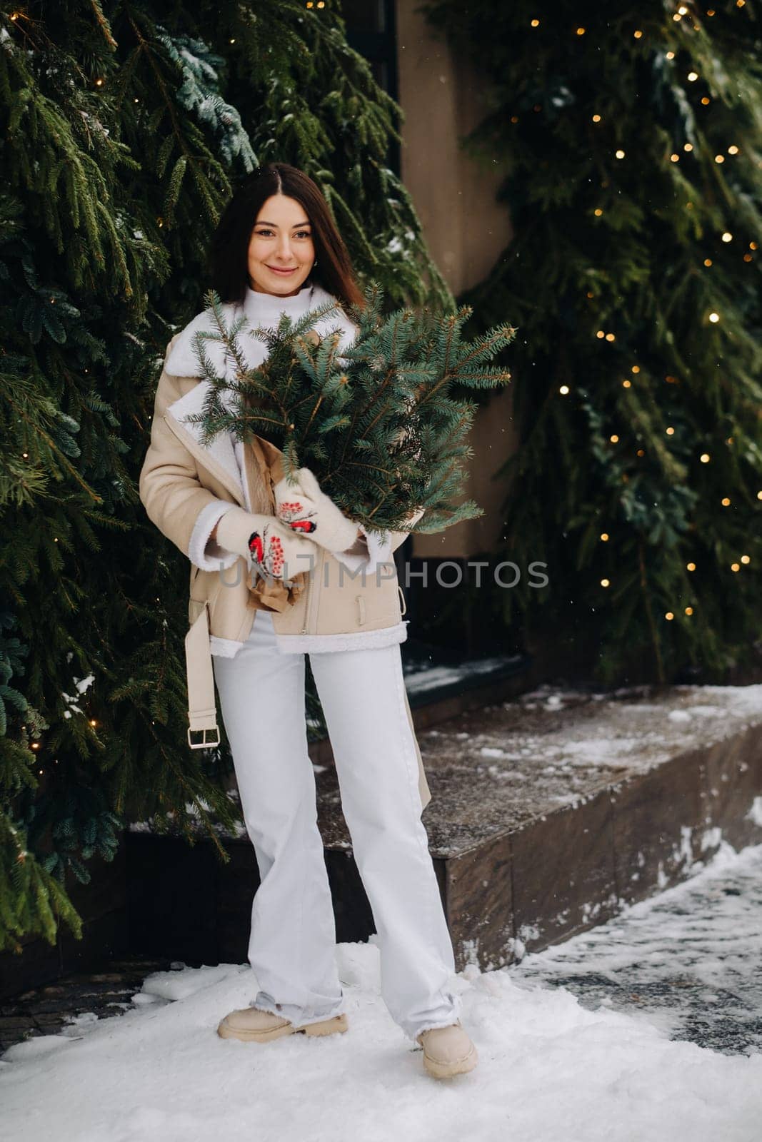 A girl with long hair in winter on the street with a bouquet of fresh fir branches.