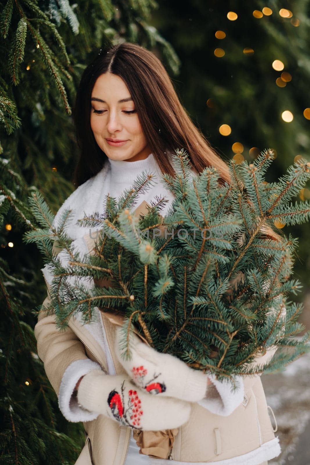 A girl with long hair in winter on the street with a bouquet of fresh fir branches.