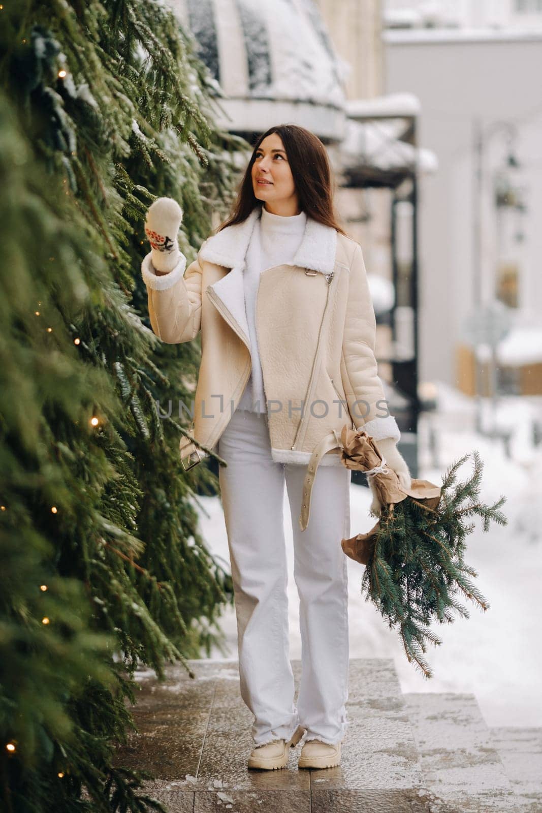 A girl with long hair in winter on the street with a bouquet of fresh fir branches.