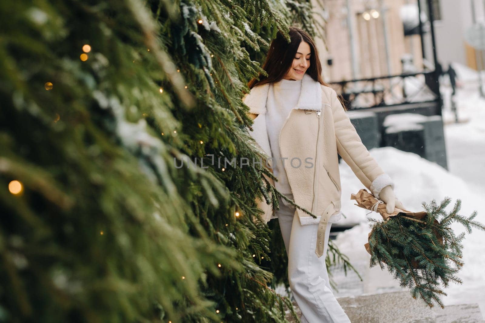 A girl with long hair in winter on the street with a bouquet of fresh fir branches.