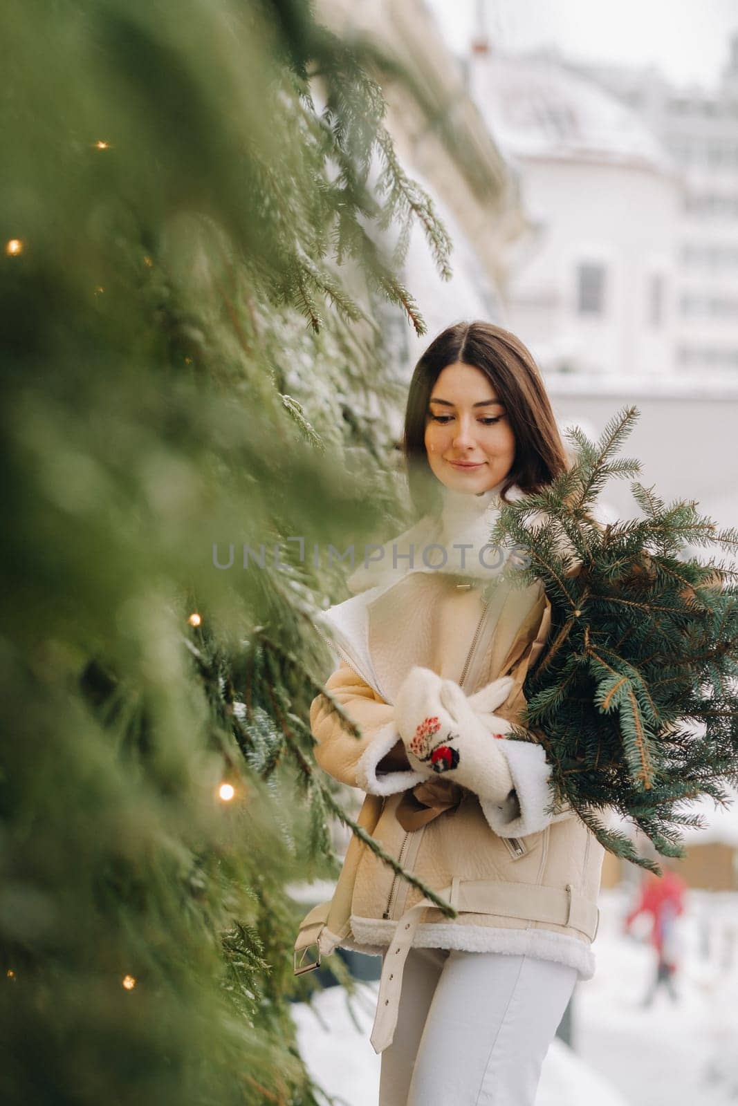 A girl with long hair in winter on the street with a bouquet of fresh fir branches.