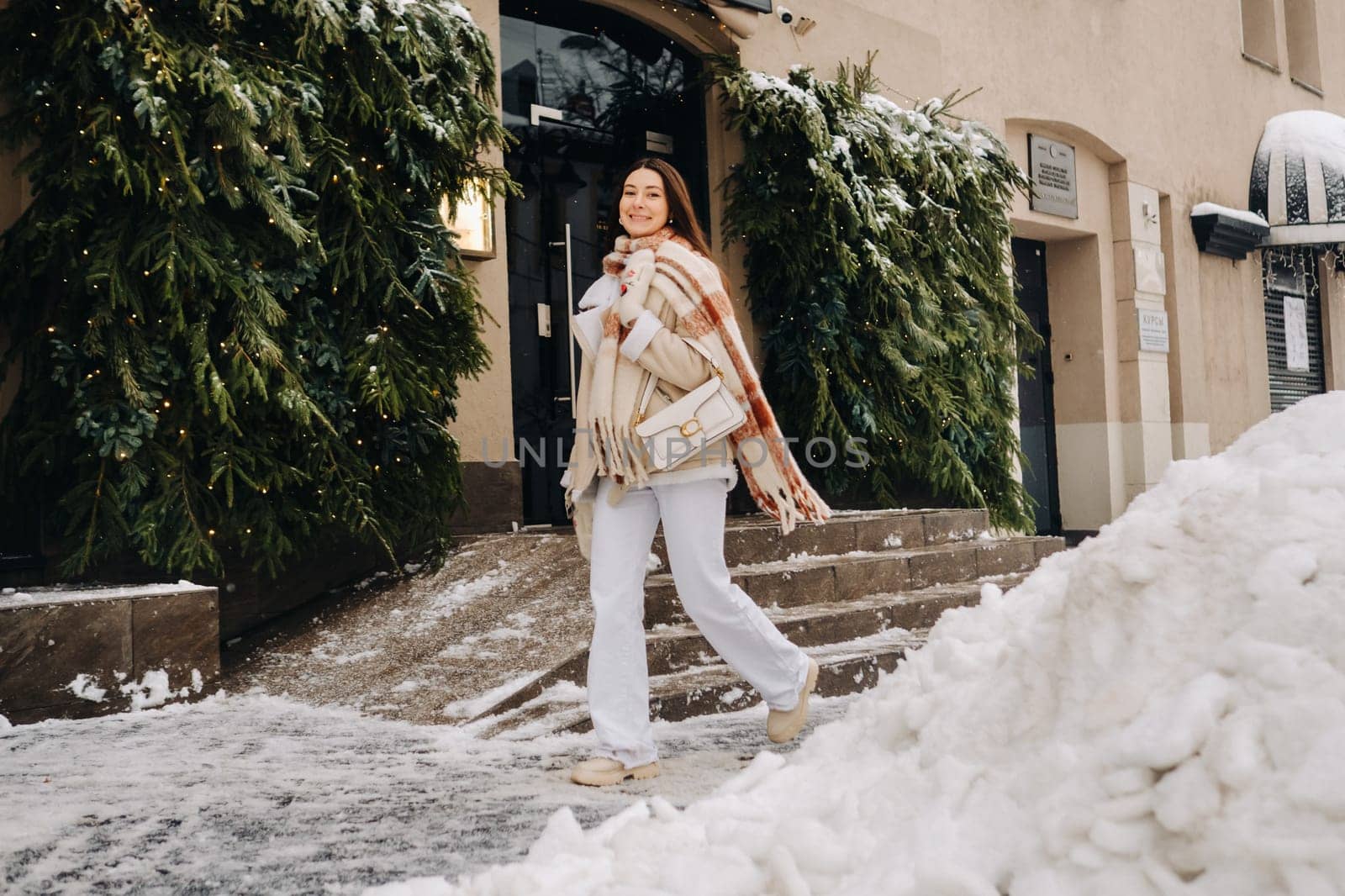 A girl with long hair in a scarf and with a white handbag walks down the street in winter by Lobachad