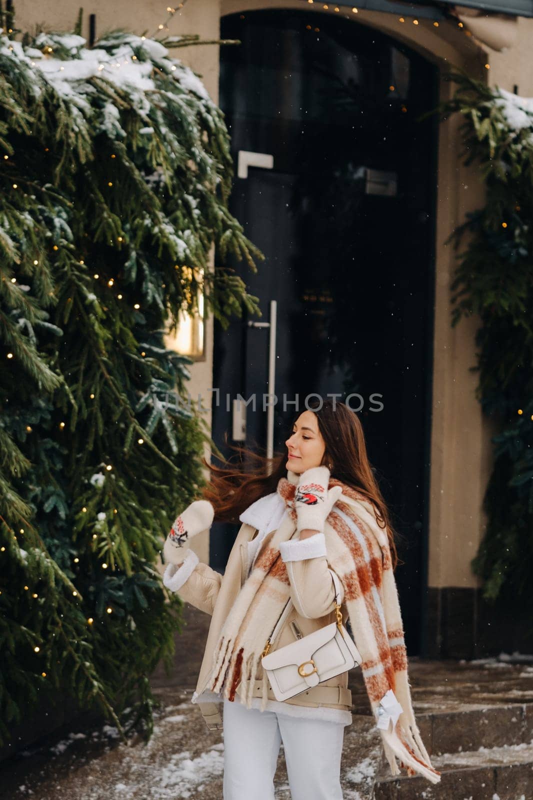 A girl with long hair in a scarf and with a white handbag walks down the street in winter.