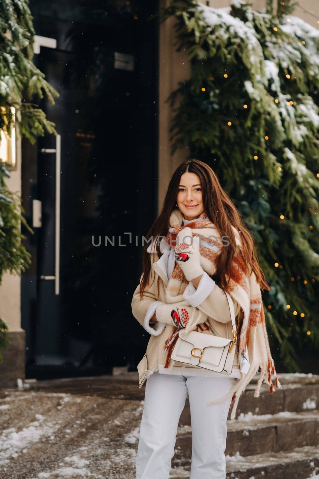 A girl with long hair in a scarf and with a white handbag walks down the street in winter.