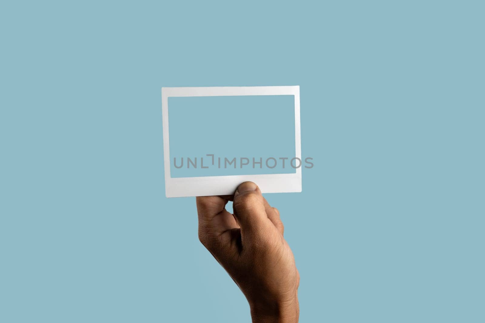 black male hand holding photo frame on isolated on light blue background by TropicalNinjaStudio