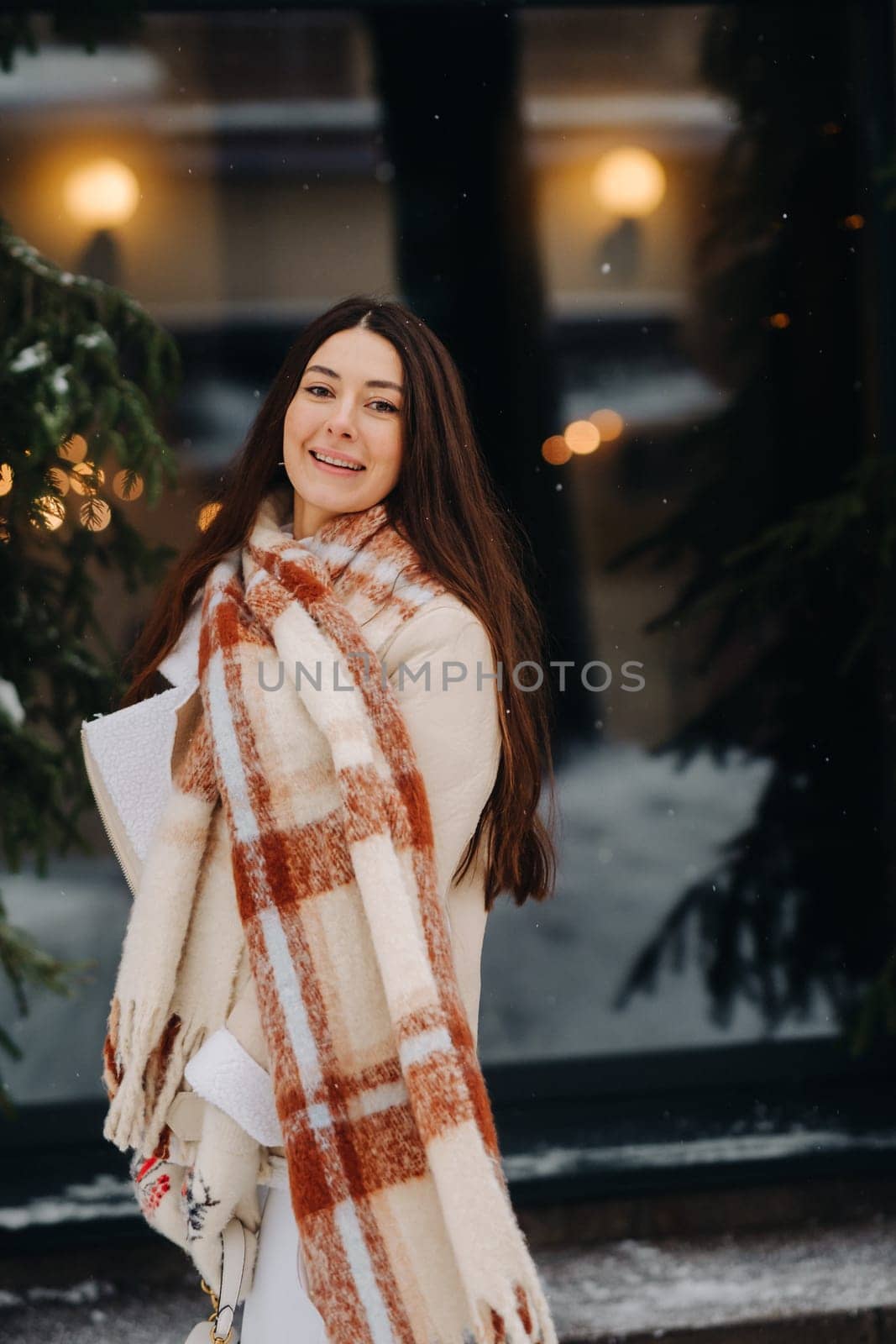 A girl with long hair in a scarf and with a white handbag walks down the street in winter by Lobachad