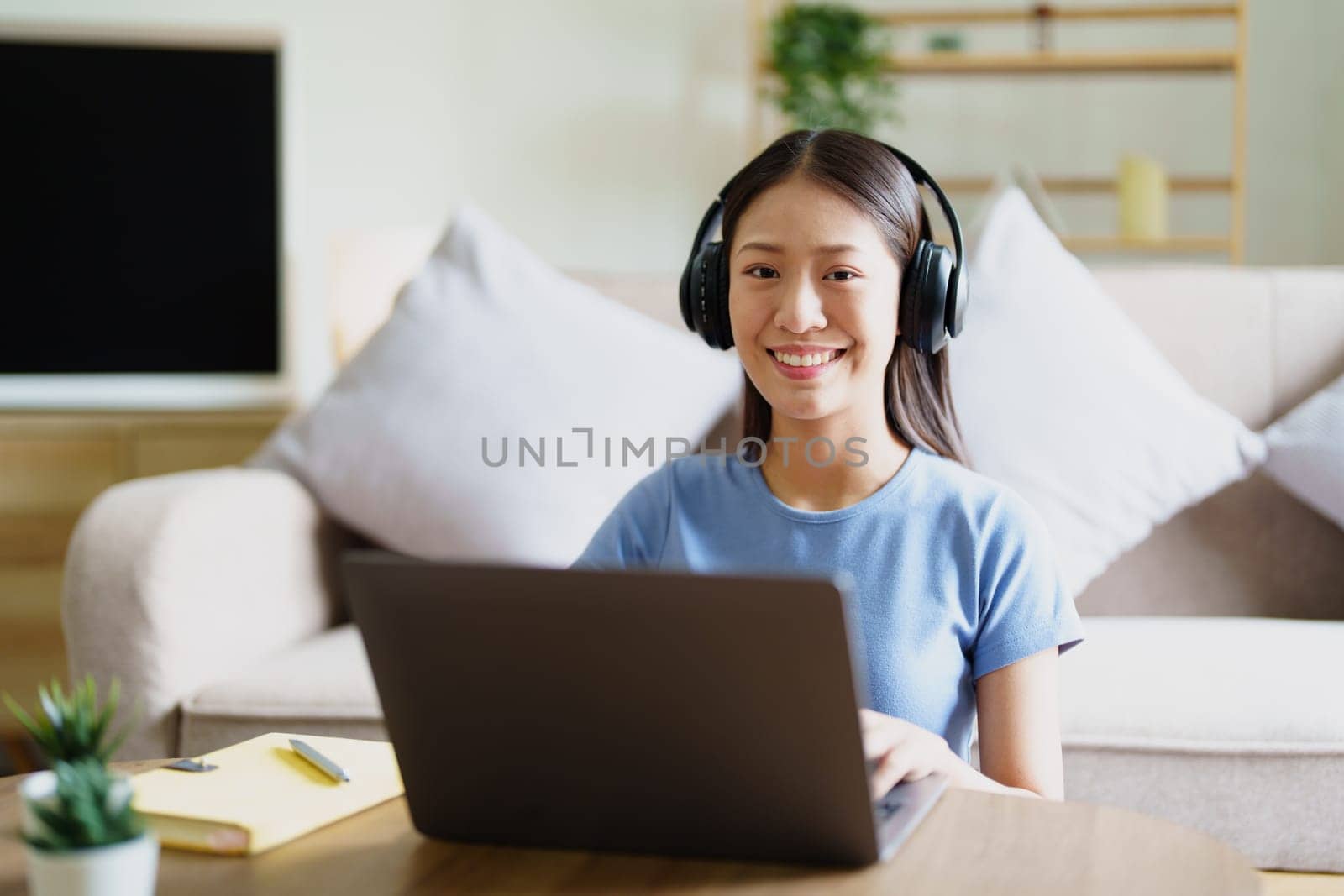 woman wearing headphones on comfortable couch listening to using computer laptop and music. by Manastrong