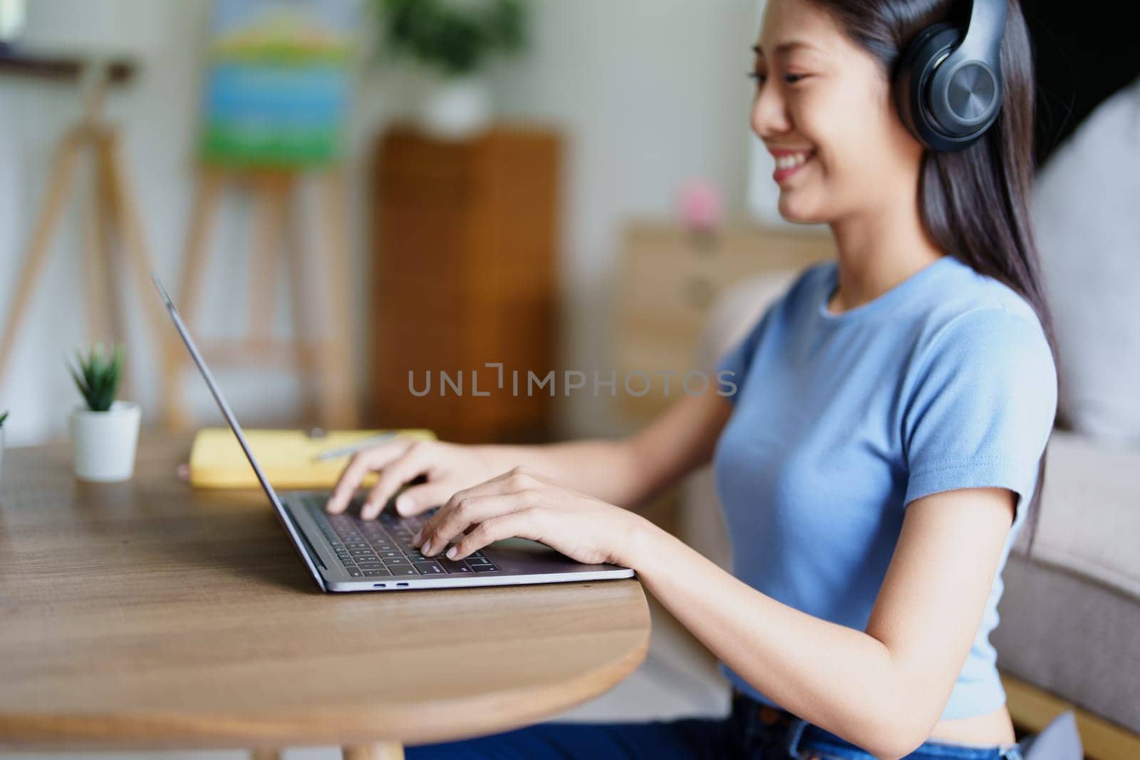 woman wearing headphones on comfortable couch listening to using computer laptop and music. by Manastrong