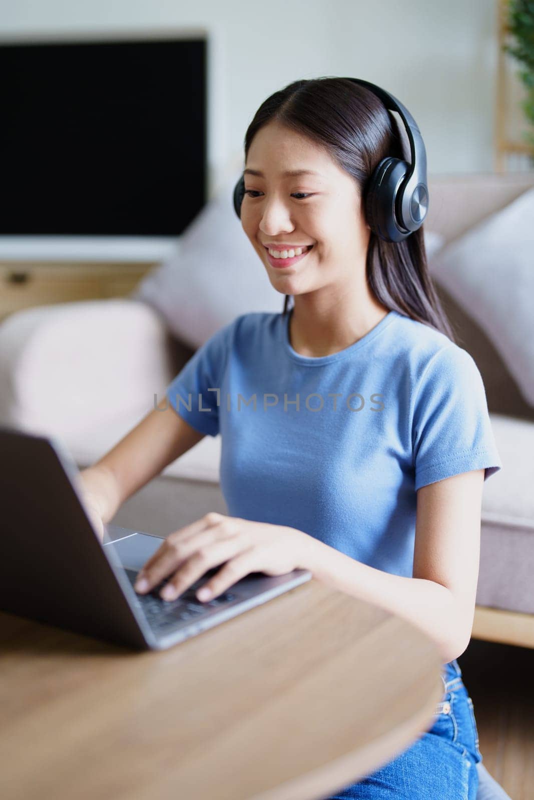 woman wearing headphones on comfortable couch listening to using computer laptop and music. by Manastrong