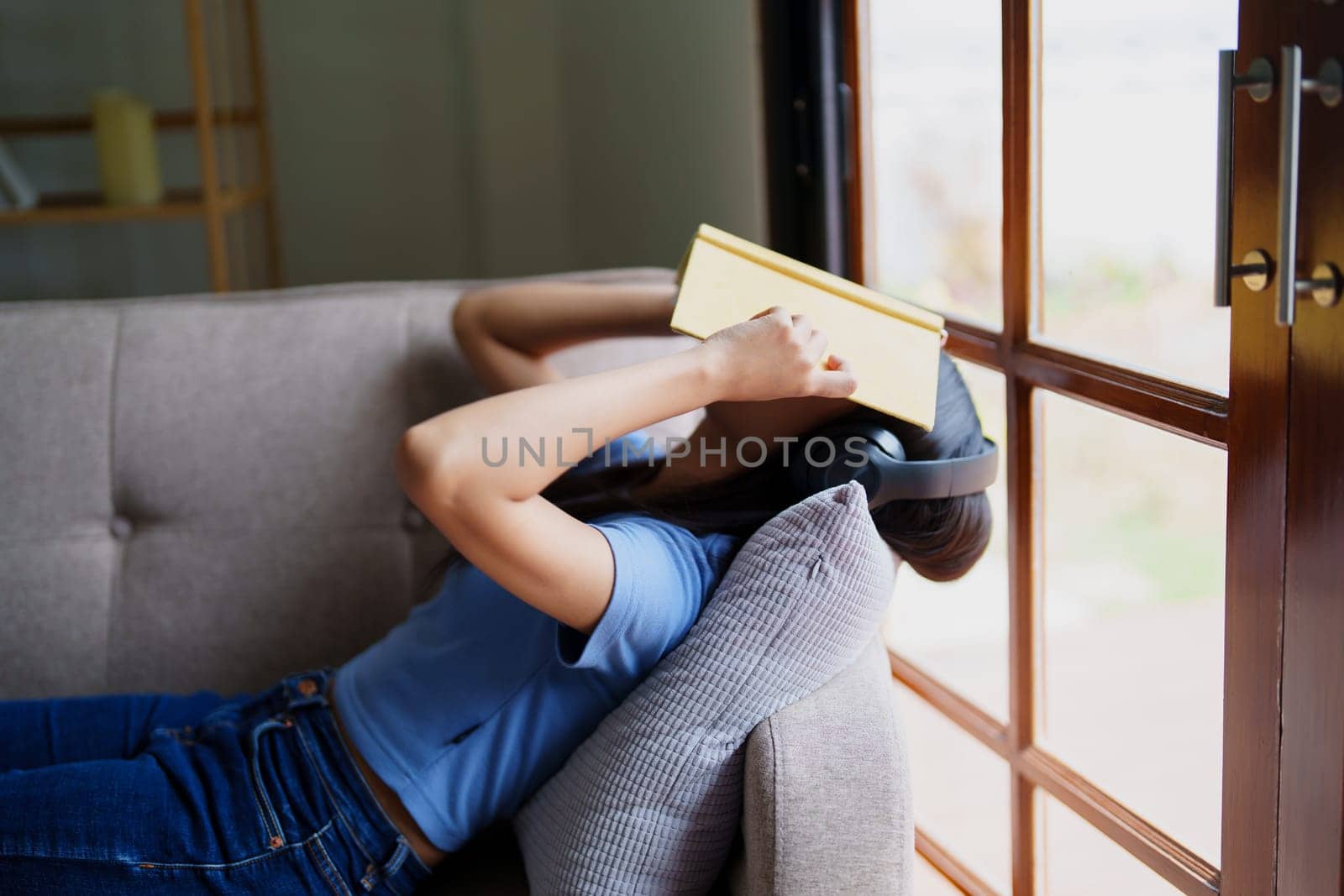 woman wearing headphones to listen music and reading notebook on sofa. by Manastrong