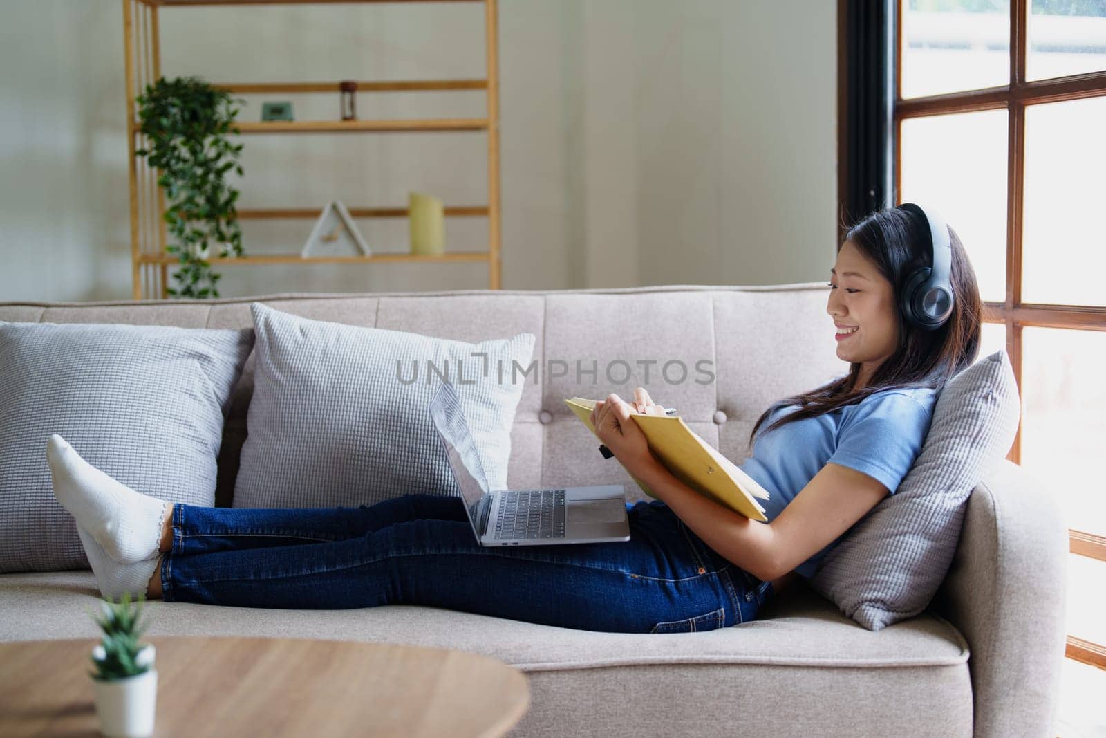 woman wearing headphones to listen music and reading notebook on sofa. by Manastrong