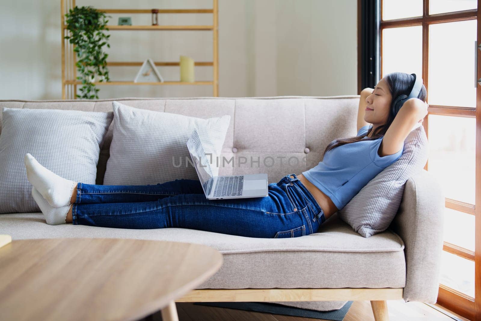 woman wearing headphones on comfortable couch listening to using computer laptop and music. by Manastrong