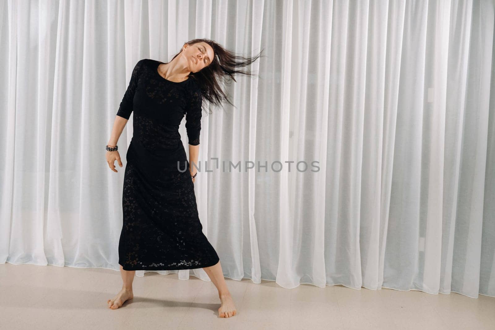 A girl in a black dress moves in a dance on a gray background. Dynamic dance by Lobachad