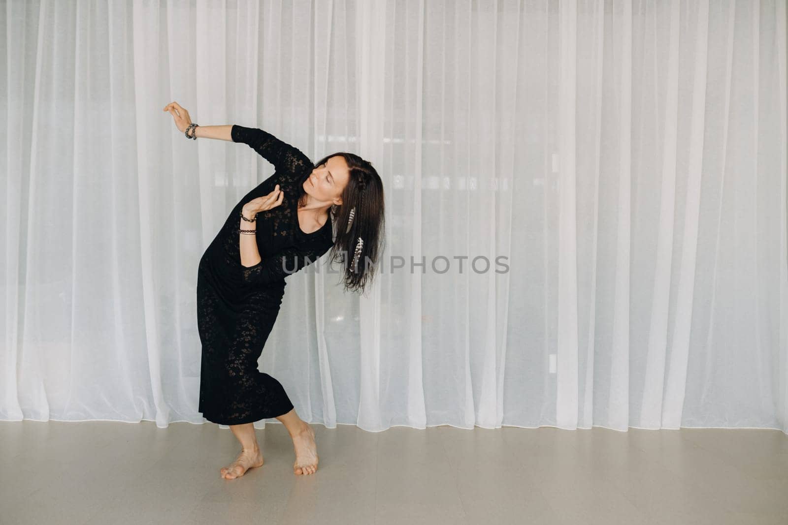 A girl in a black dress moves in a dance on a gray background. Dynamic dance,