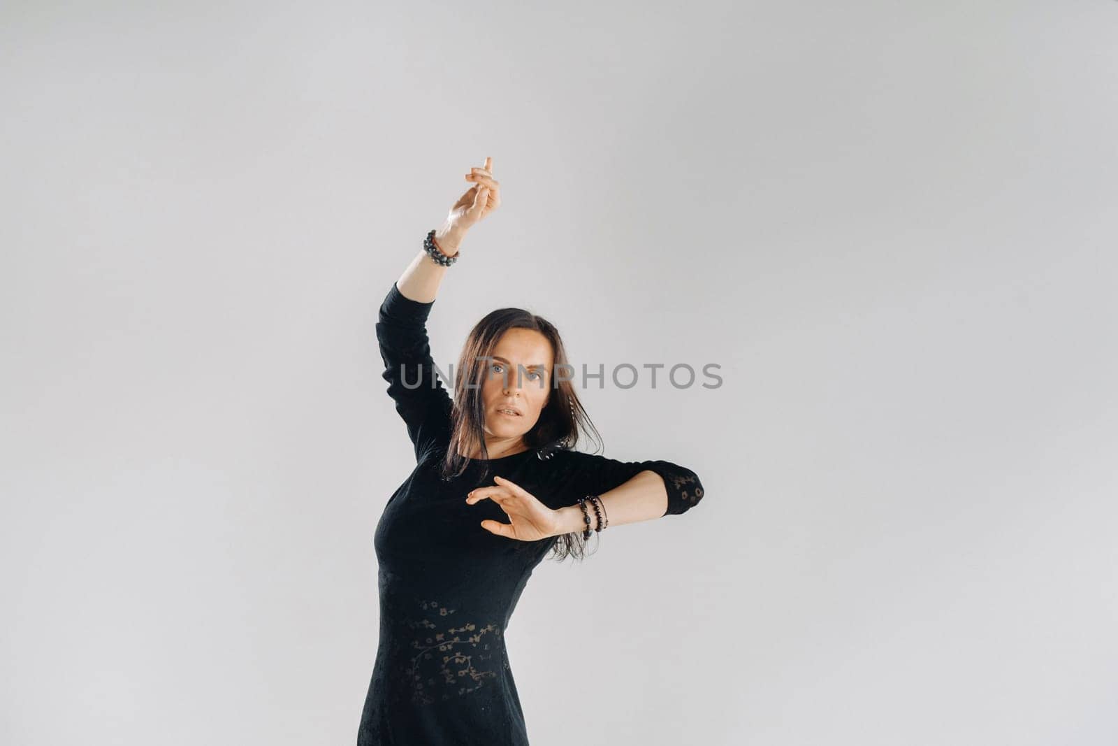 A girl in a black dress moves in a dance on a gray background. Dynamic dance,