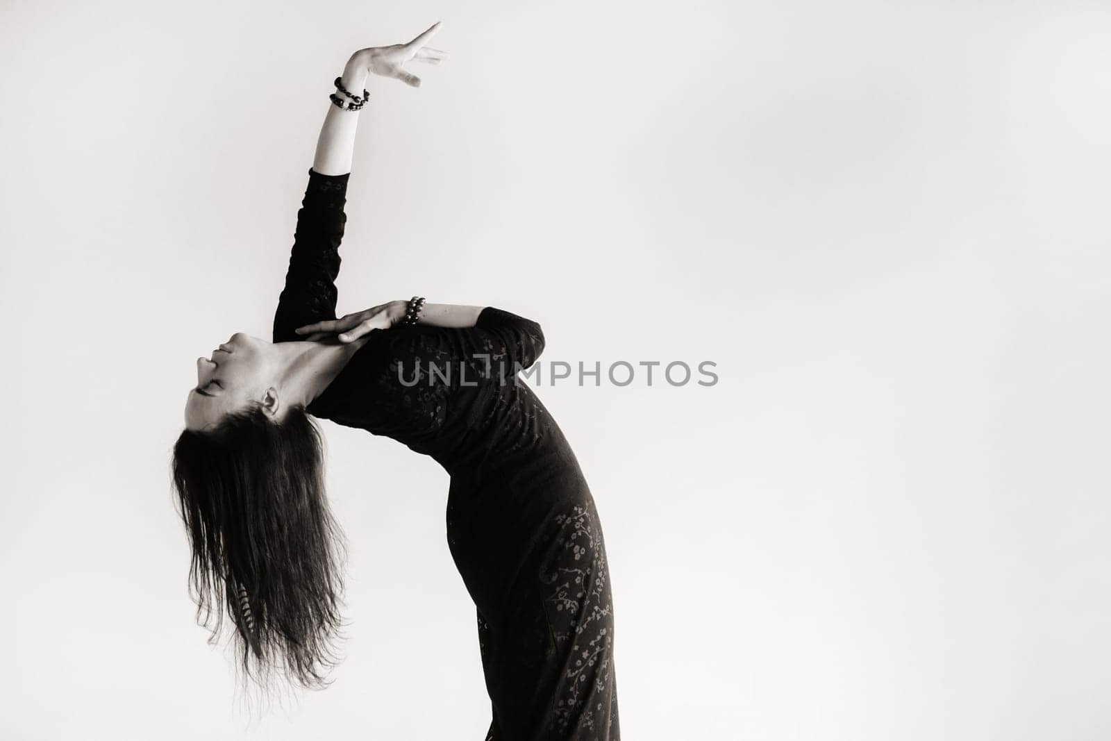 A girl in a black dress moves in a dance on a gray background. Dynamic dance,