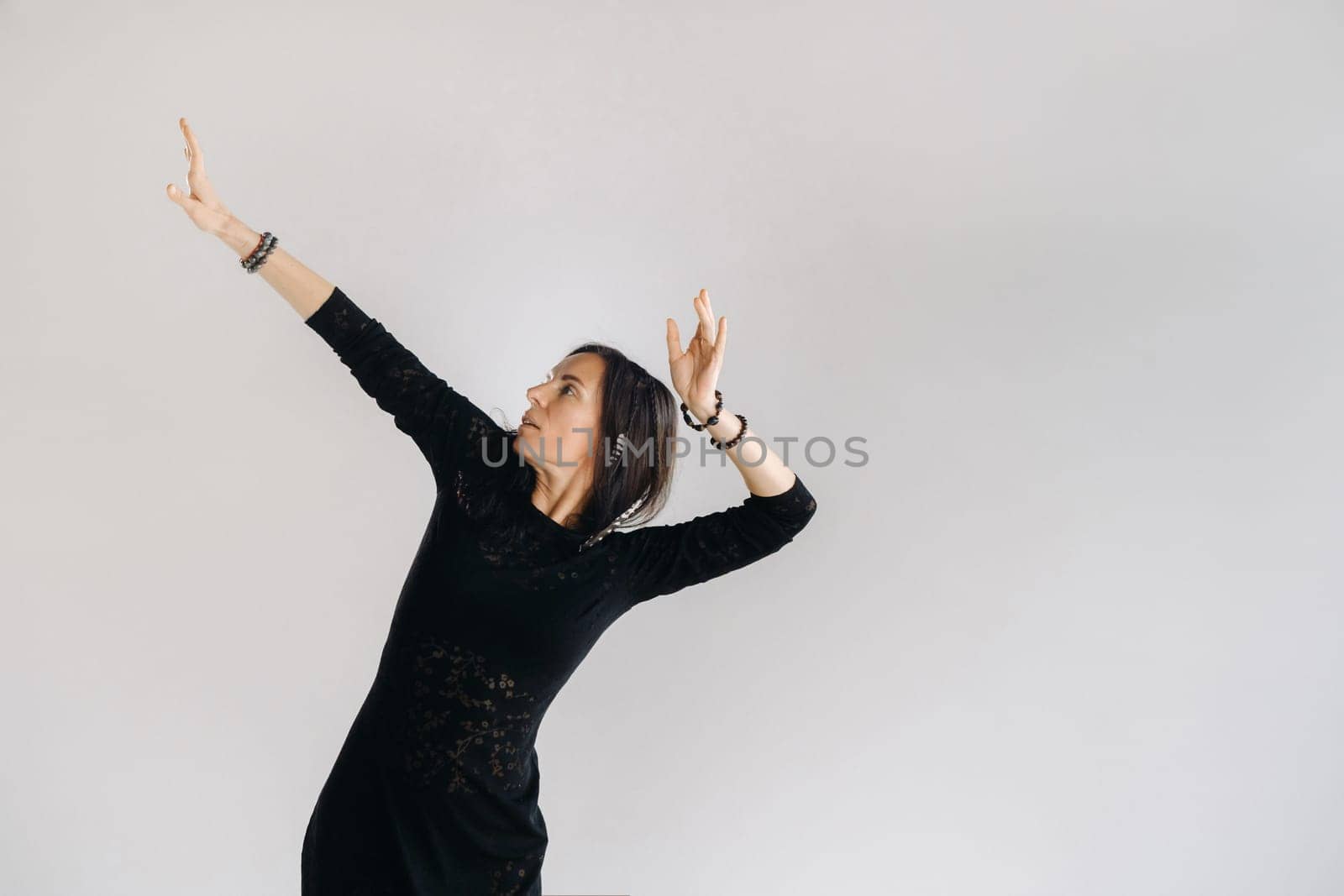 A girl in a black dress moves in a dance on a gray background. Dynamic dance,