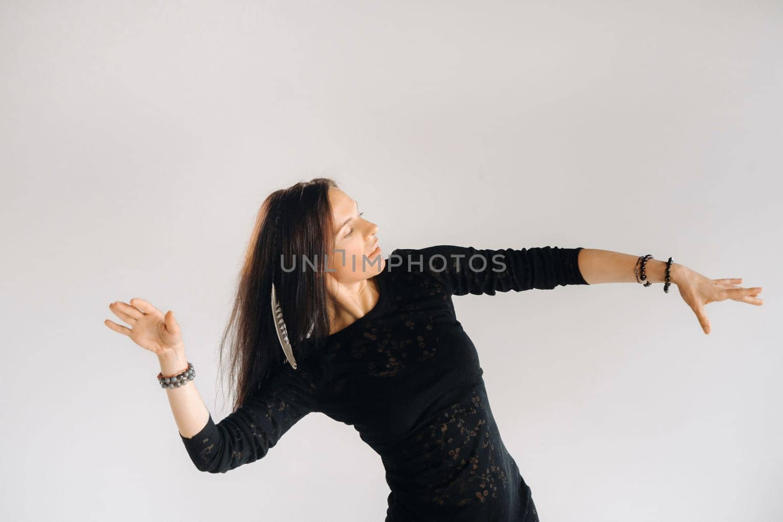 A girl in a black dress moves in a dance on a gray background. Dynamic dance,