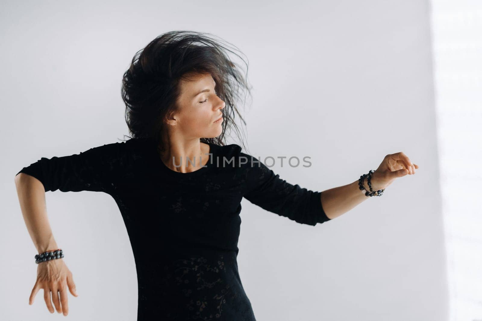 A girl in a black dress moves in a dance on a gray background. Dynamic dance,