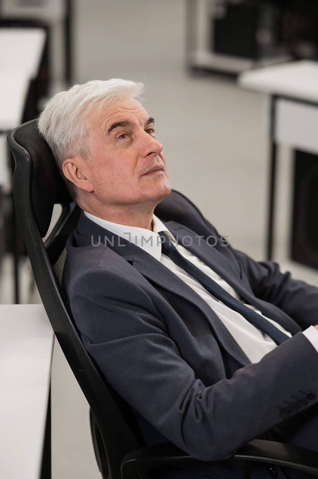Portrait of a pensive mature business man sitting in a chair in the office. Vertical photo