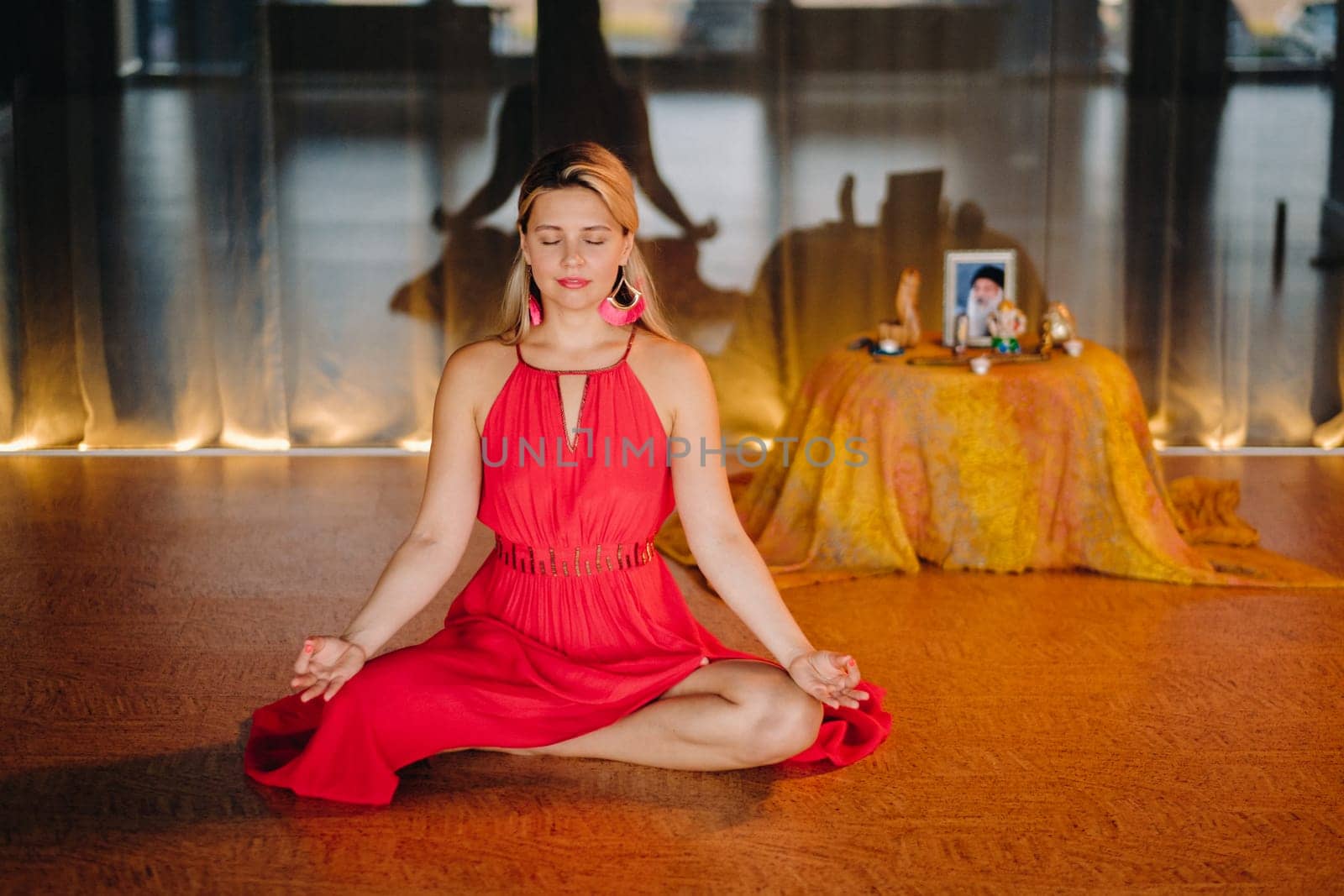 Meditation and concentration. a woman in a red dress, sitting on the floor with her eyes closed, is practicing medicine indoors. Peace and relaxation.