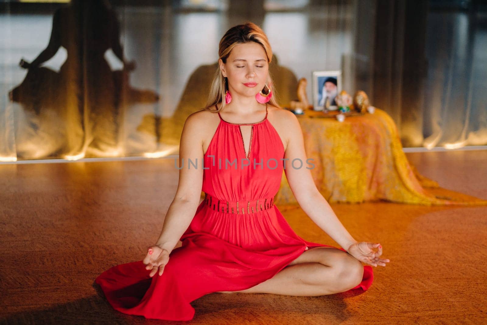 Meditation and concentration. a woman in a red dress, sitting on the floor with her eyes closed, is practicing medicine indoors. Peace and relaxation by Lobachad