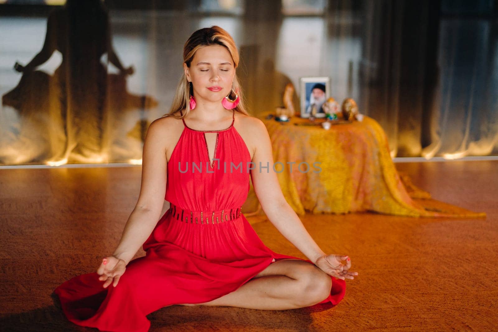 Meditation and concentration. a woman in a red dress, sitting on the floor with her eyes closed, is practicing medicine indoors. Peace and relaxation by Lobachad