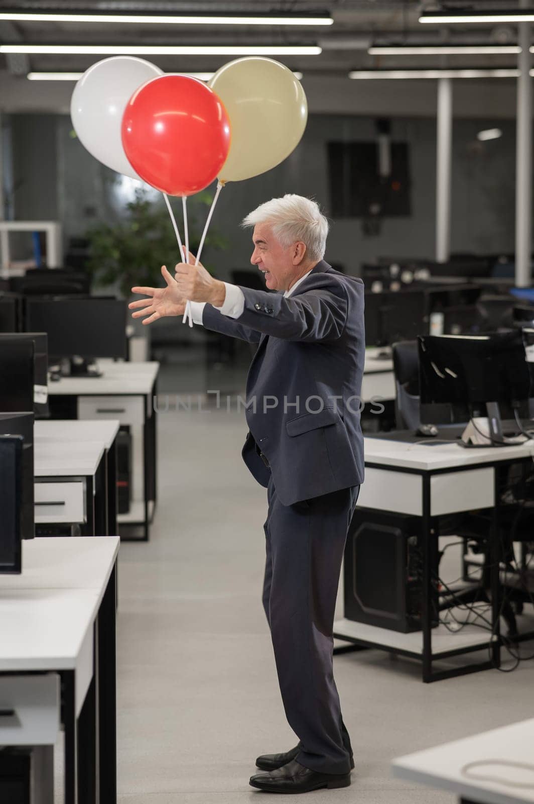 Portrait of a cheerful mature business man holding balloons in the office. Vertical photo. by mrwed54