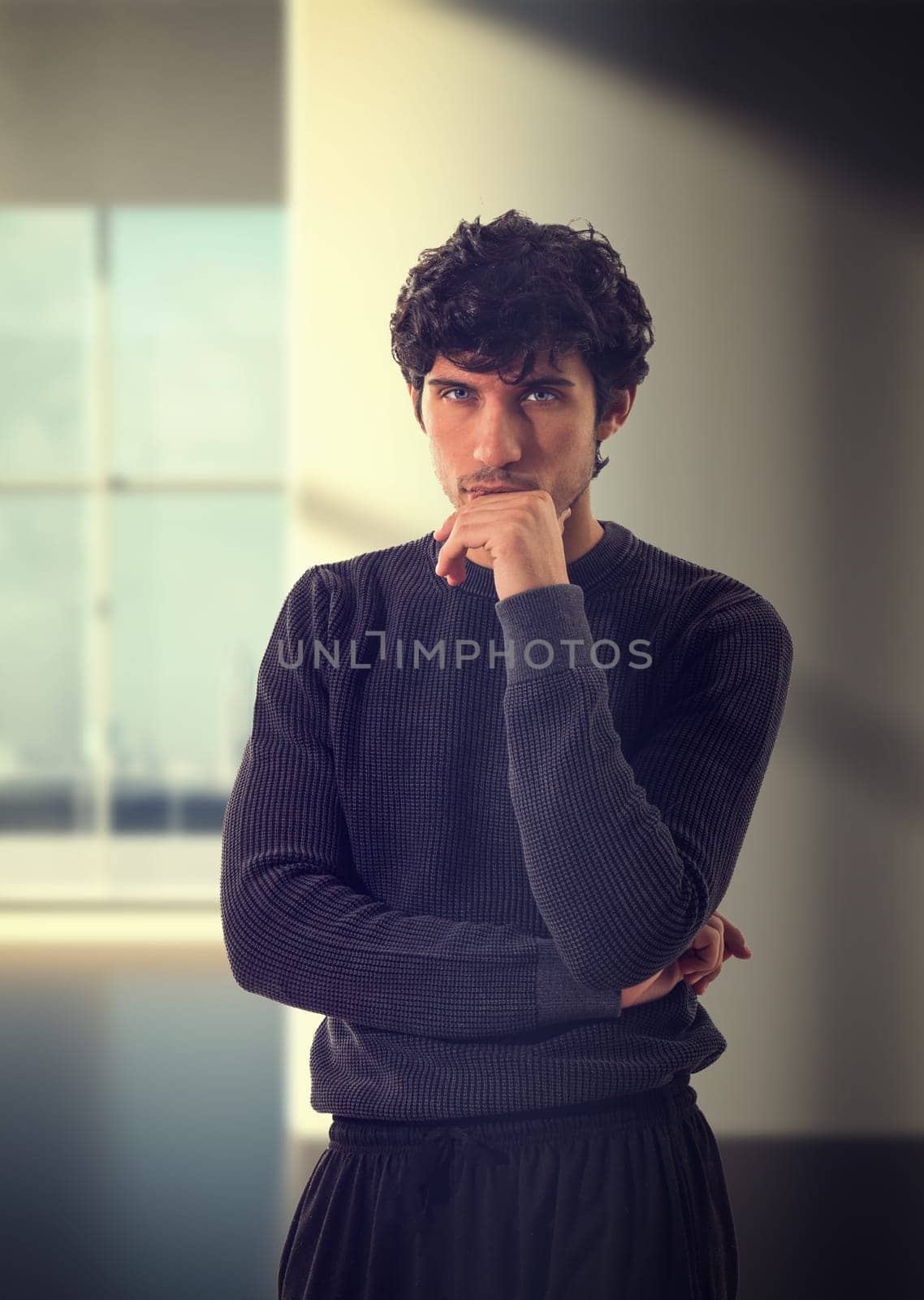 A man standing in a room with his hand on his chin. A Man Reflecting in a Thoughtful Pose