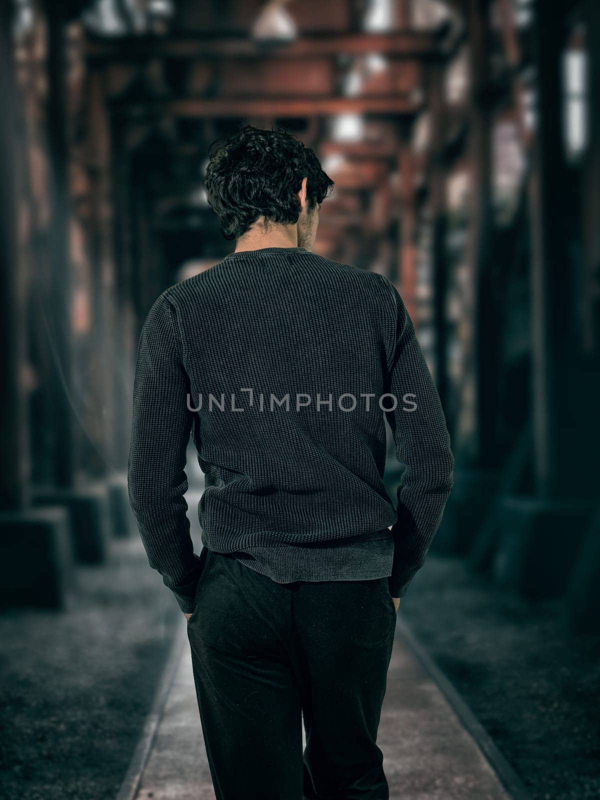 A man walking down a dark alley way, unrecognizable, with hands in his pockets